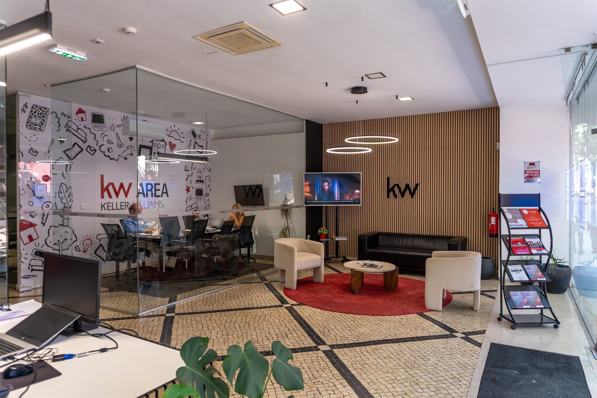 Piso 0 da KW Area visto da entrada, com a sala de trabalho envidraçada à esquerda, o logótipo KW AREA no vidro e a zona de estar ao fundo