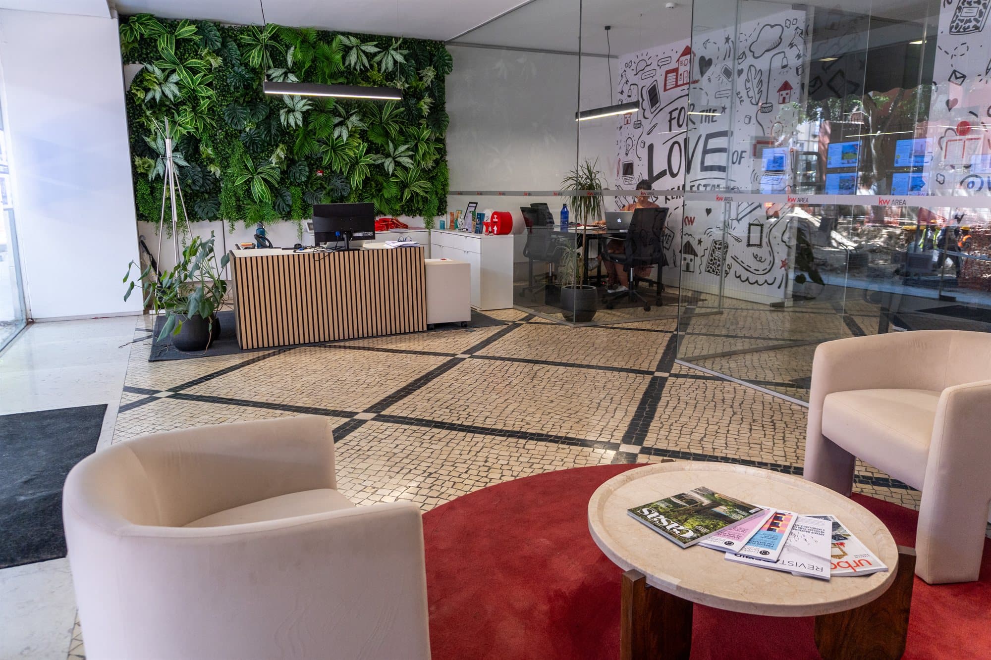Recepção do piso 0 da KW Area, com balcão de ripas de madeira, parede de plantas e chão em calçada portuguesa