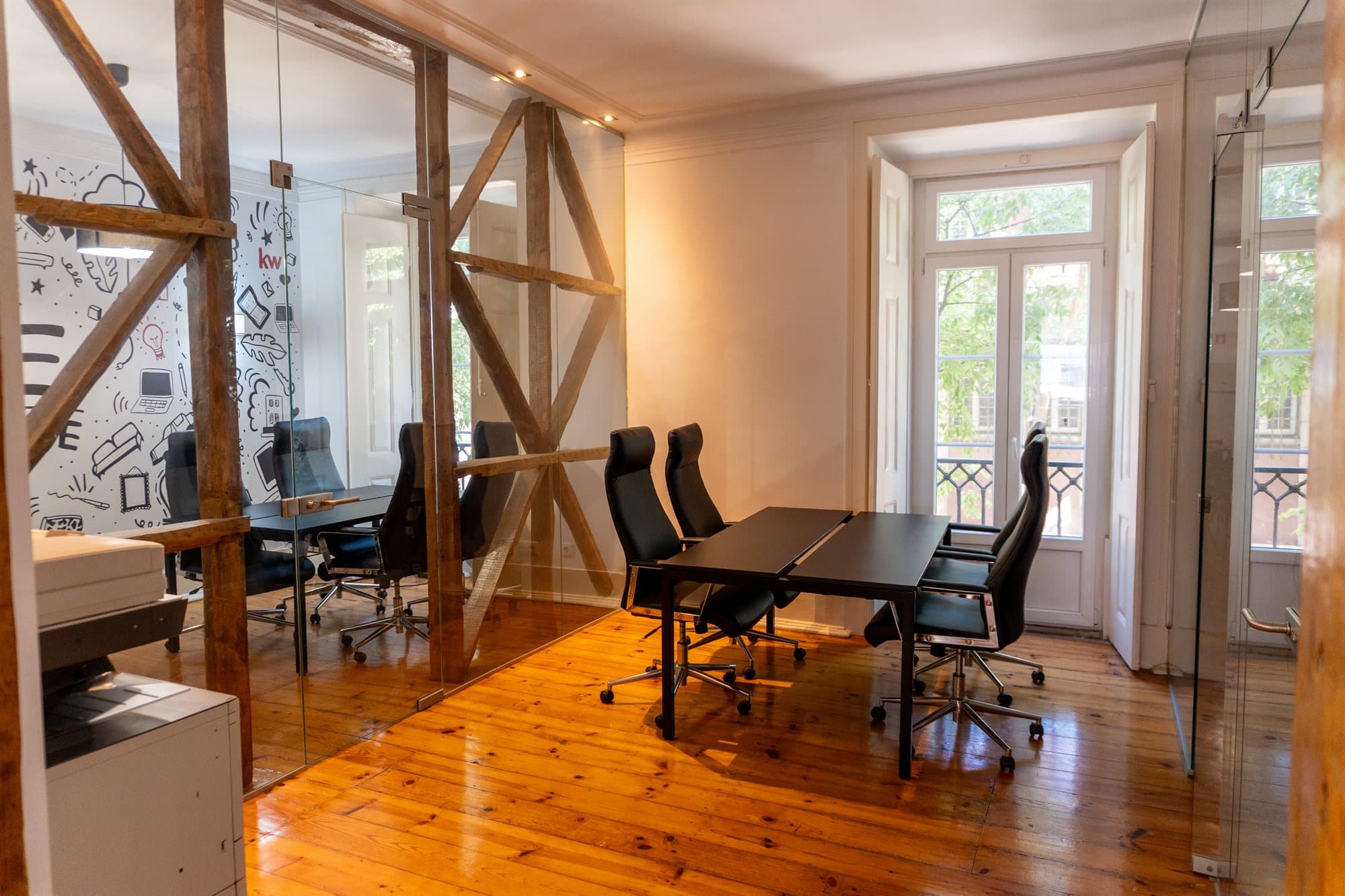 Sala de reuniões do piso 1 da KW Area, com soalho de madeira, vigas antigas à vista e porta de sacada para a rua