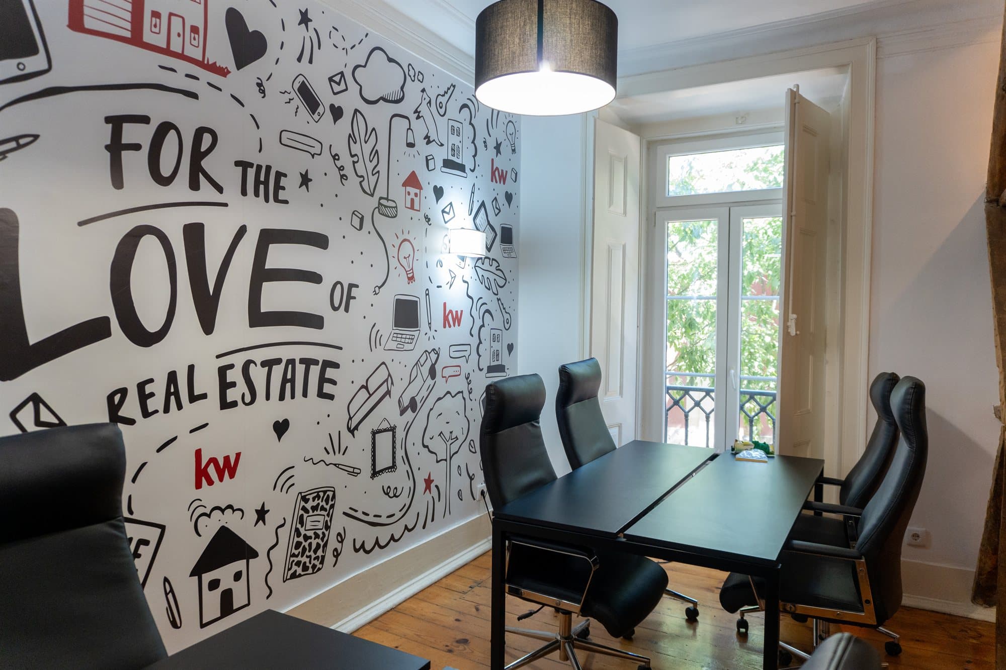 Sala de reuniões do piso 1 da KW Area, com o mural For the love of real estate a ocupar a parede e a janela aberta para as árvores